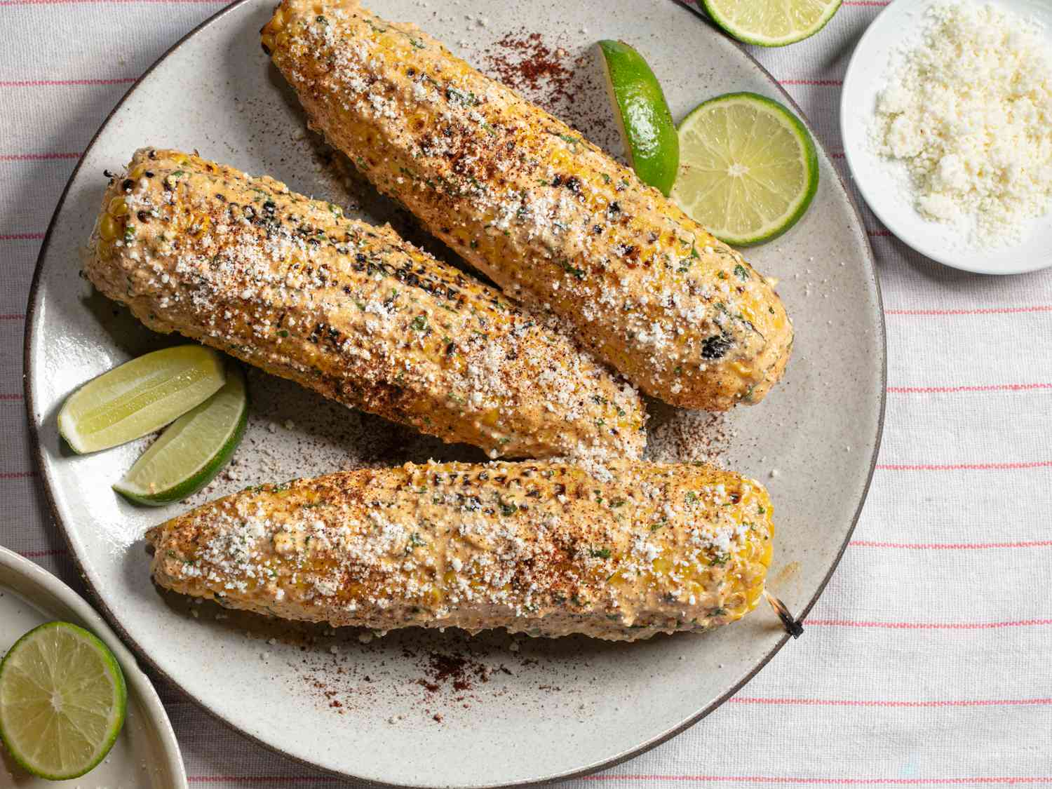 Elotes (grilled Mexican street corn) on a plate with limes and chili powder