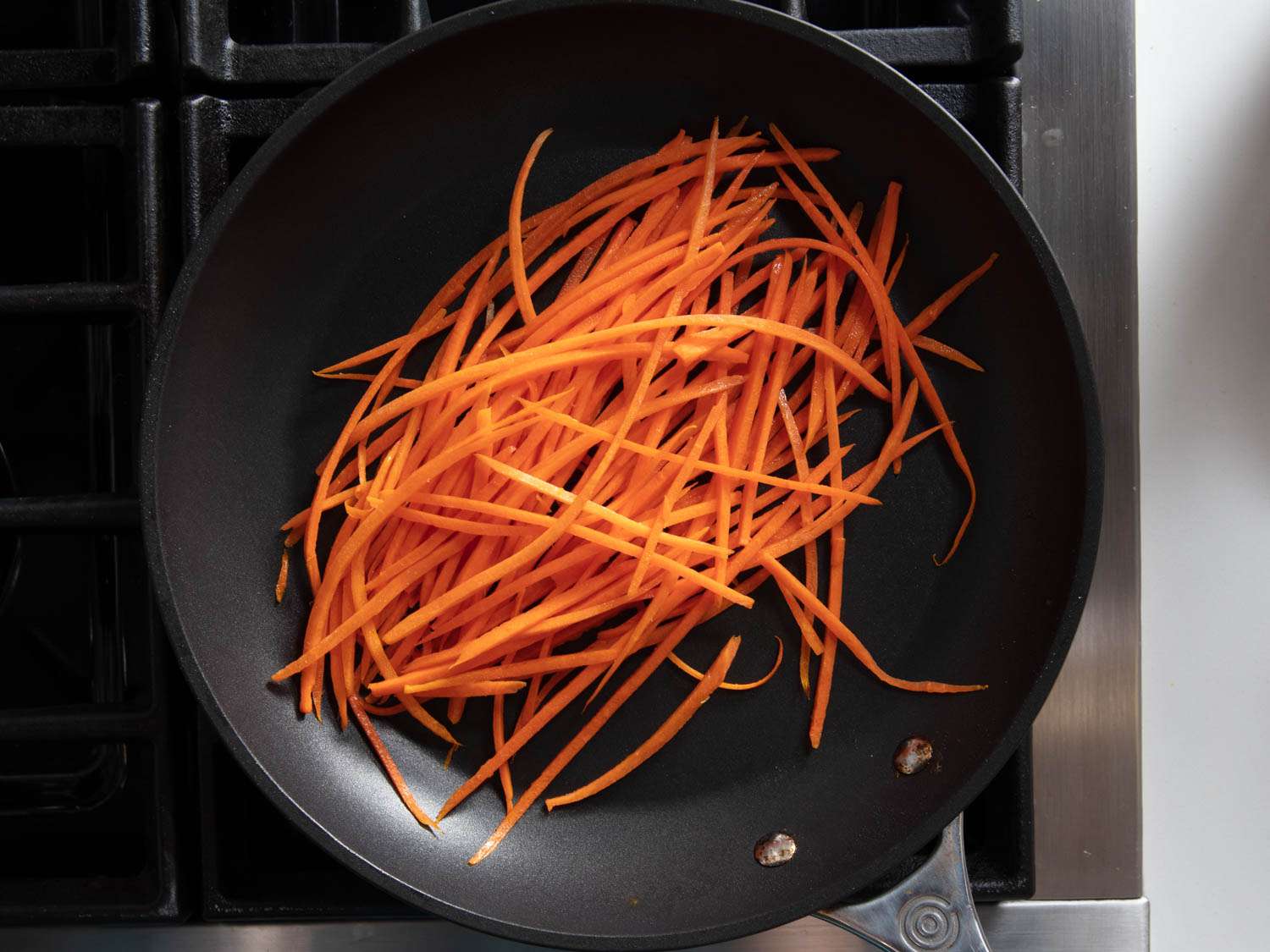 Overhead shot of very long and skinny strips of carrot in a nonstick skillet.