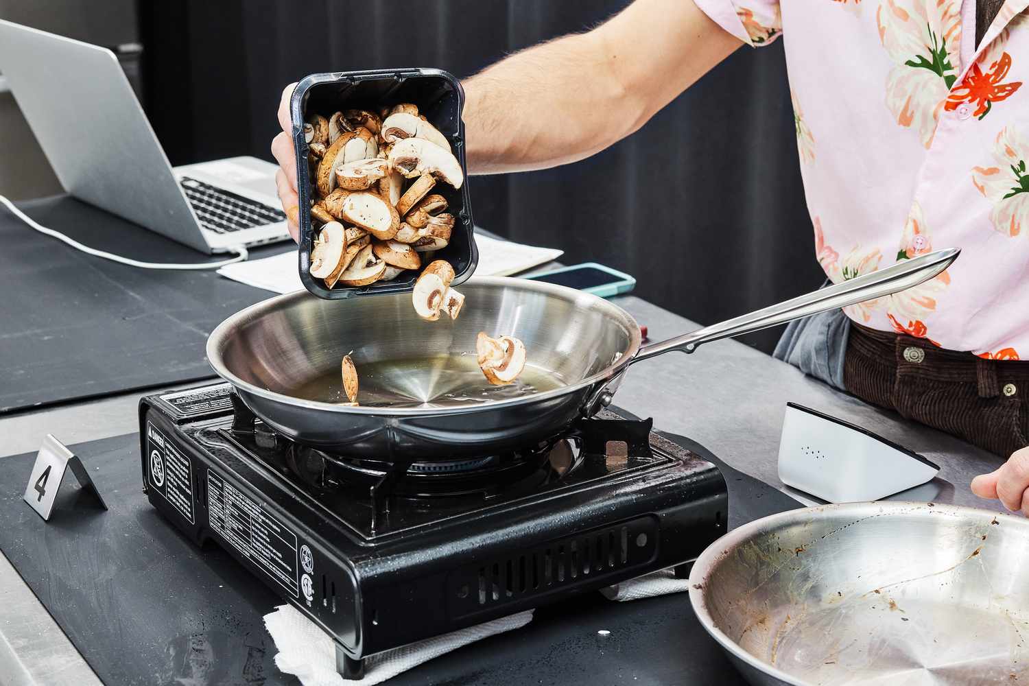 a person pouring sliced mushrooms in a stainless steel skillet