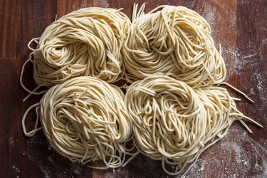 Freshly cut homemade ramen noodles in four nests on a flour-dusted wood cutting board