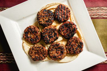 Overhead view of losh kebabs on pita on a white plate on a nicely textured, striped fabric