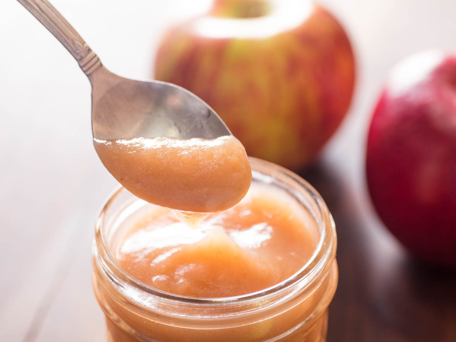 一个勺子从罐子里舀出一些苹果酱的特写，背景是整个苹果