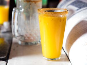A rimmed pint glass of bright-orange pulque.