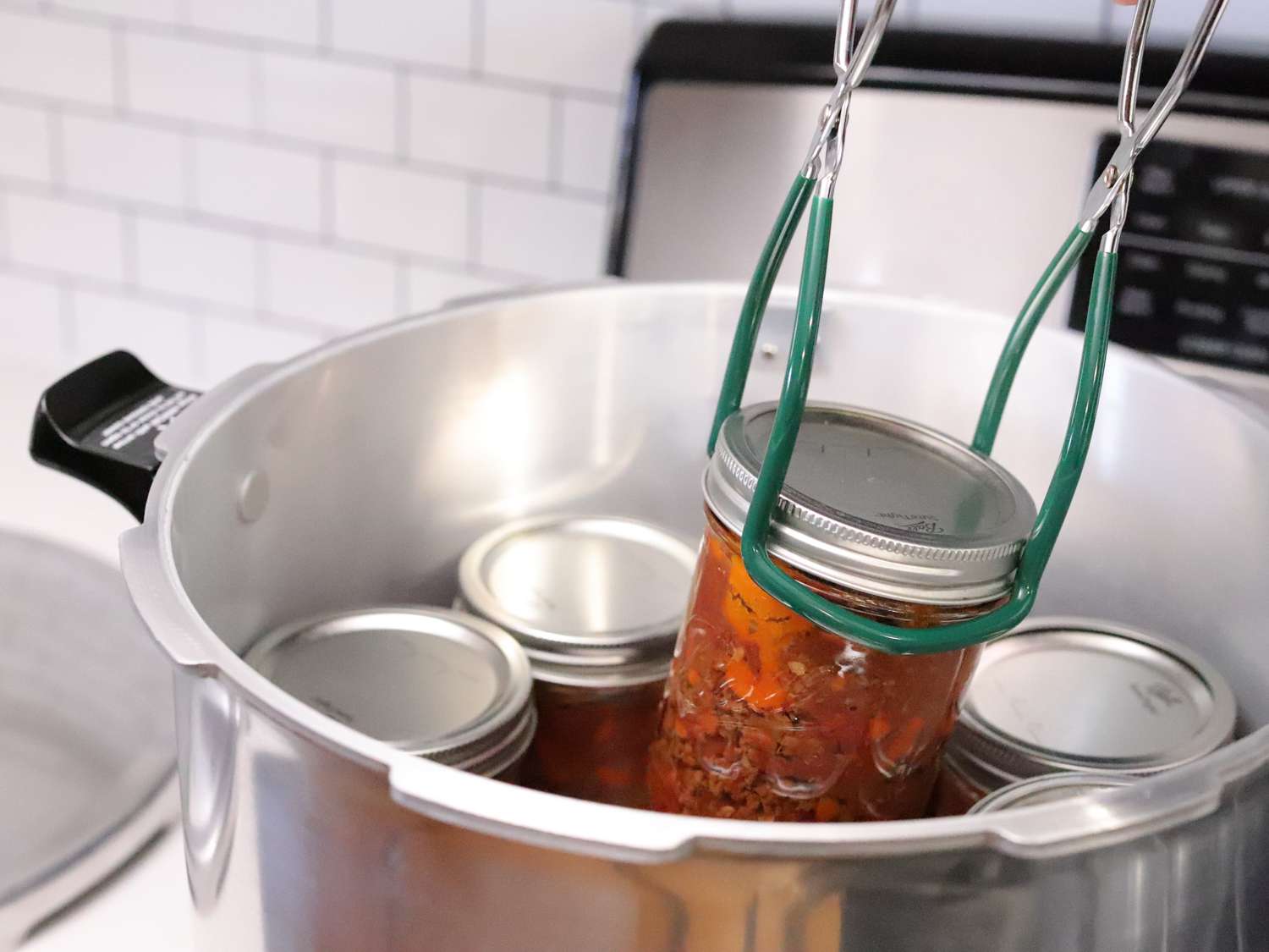 a jar of tomatoes getting lowered into a pressure canner