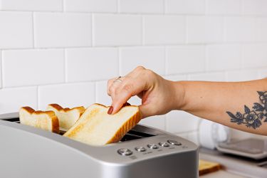 A hand pulling a lightly toasted slice of white bread out of a toaster