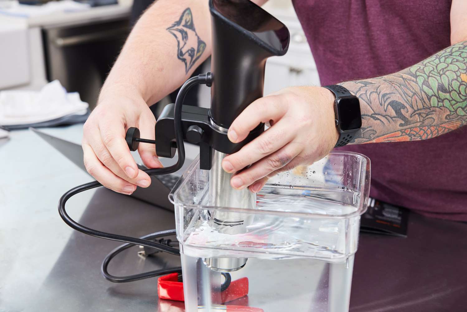 A hand using placing a sous vide machine into a cambro container filled with water