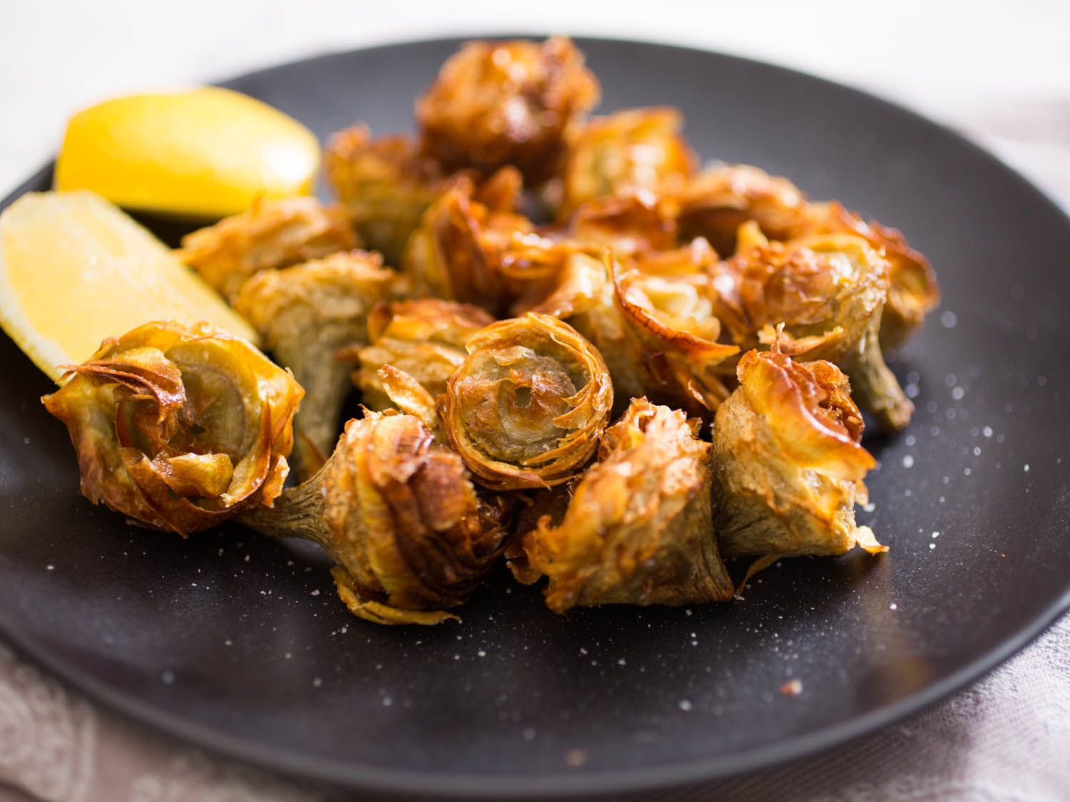 Golden fried salted artichoke hearts plattered with two lemon wedges.