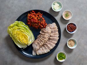 A platter of bossam, complete with sliced pork belly, fresh cabbage leaves, and an array of condiments.