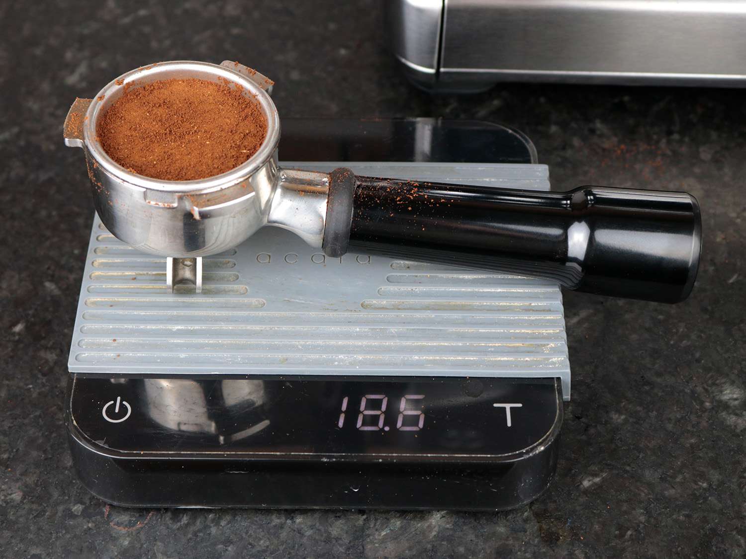 a portafilter rests on a scale showing how much coffee is tamped in the filter basket