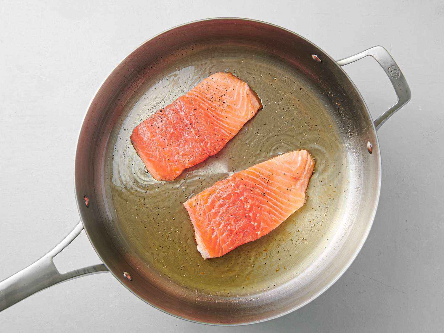 Salmon cooking skin-side-down in oil inside a 12-inch stainless steel skillet