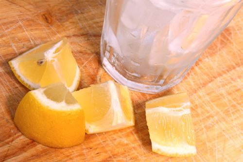 Overhead photo of ice in glass next to lemon wedges on wooden surface.