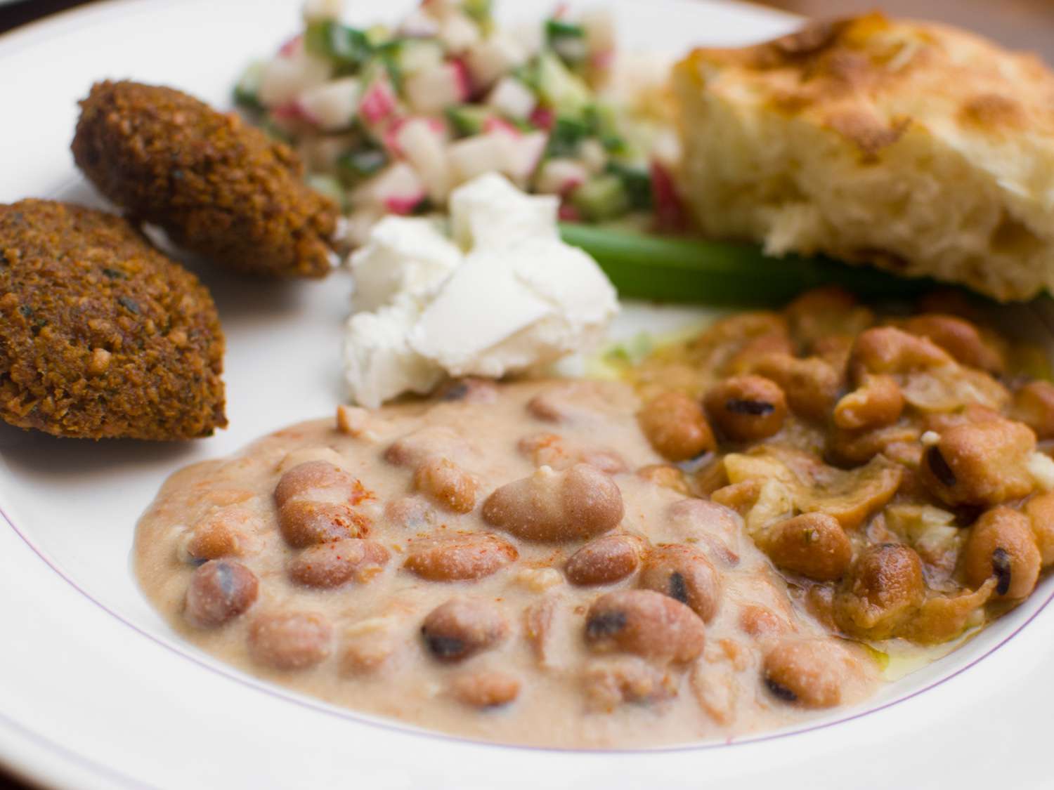 A plate of ful medames served with falafel, labne, side salad and a piece of toasted bread.