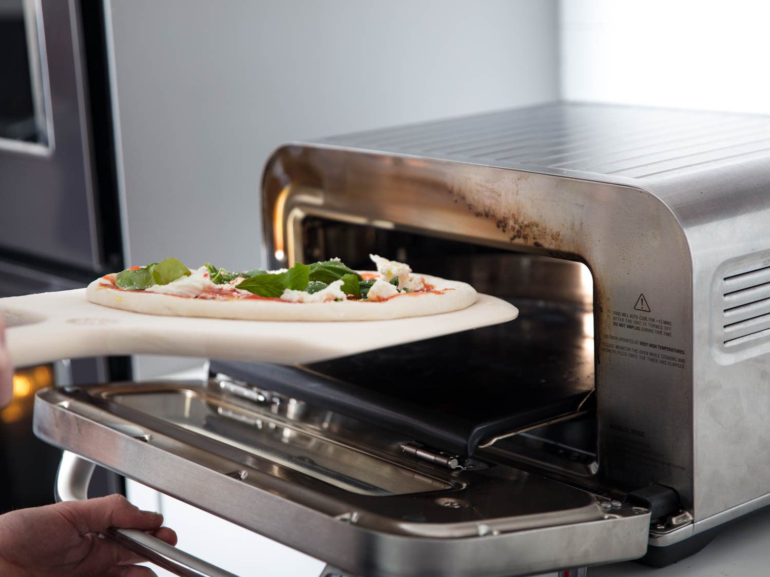 Sliding a margherita pizza into the Breville oven.