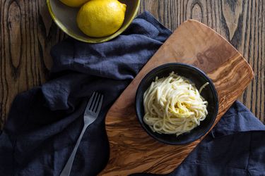A bowl of pasta al limone on an olive wood cutting board with a dark blue linen napkin.