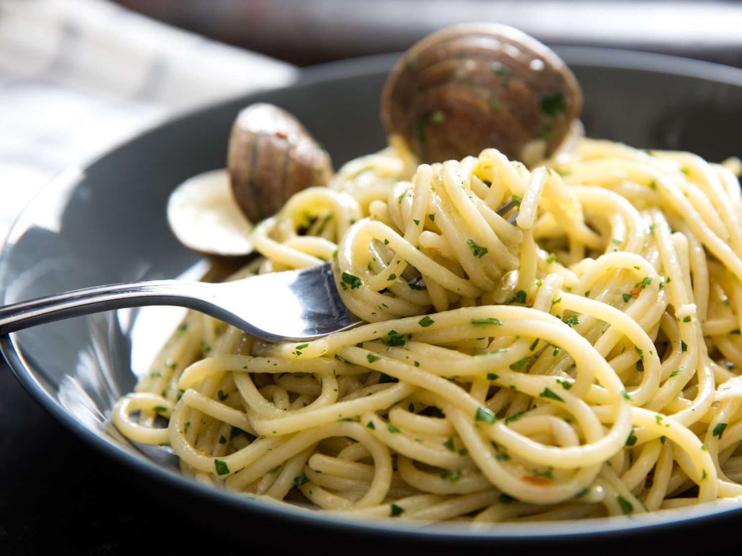 Closeup of a fork, twirled with herb-flecked spaghetti, resting on a serving of spaghetti alle vongole in bianco.