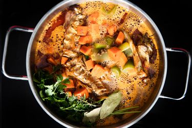俯视图烤火鸡骨头，棕色的蔬菜，和香草炖在汤锅