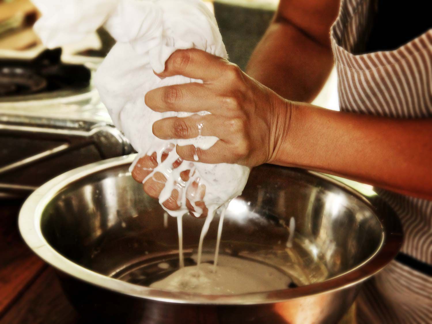 手挤压新鲜的椰子通过厨房毛巾在金属碗上做椰奶。