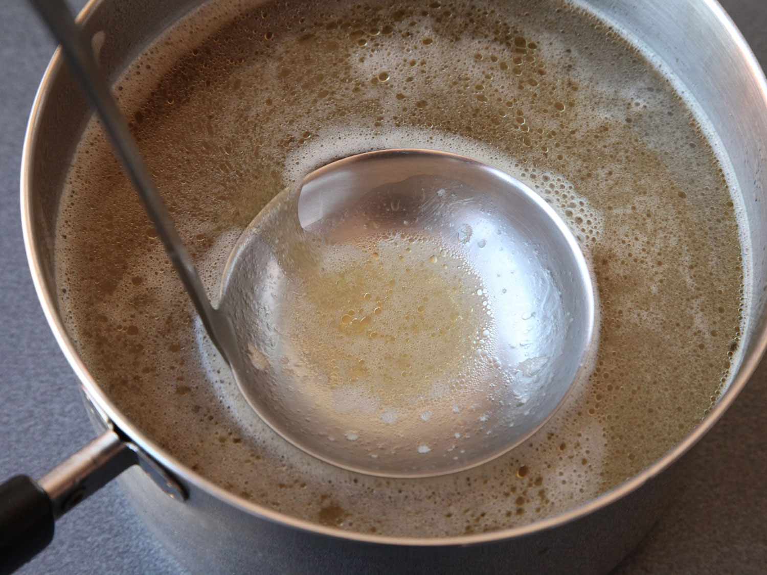 用勺子从高压锅越南粉汤顶部撇去杂质。