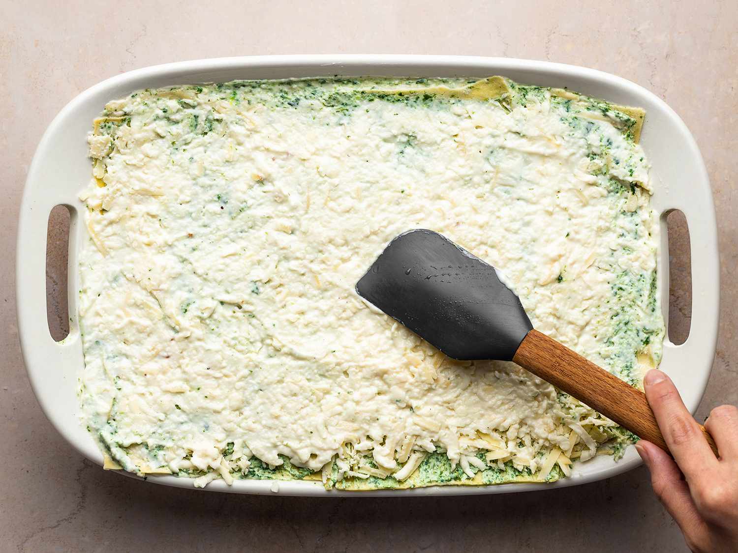 The lasagna in a baking dish with the final layer of cheese being applied to the surface.