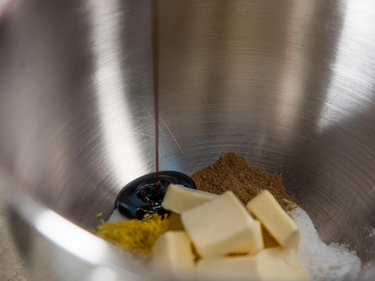 Butter, sugar, etc. have been added to the bowl of a stand mixer. Molasses is being poured in.