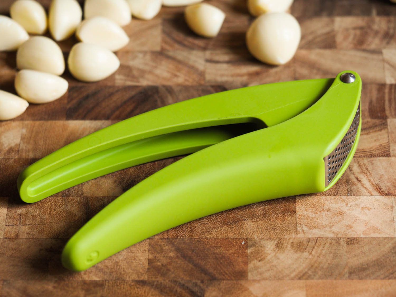 A garlic press on cutting board next to garlic cloves.