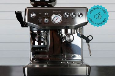 an espresso machine with a built-in grinder sits on a counter in front of a tiled wall