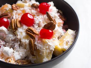 A bowl of ambrosia, a fruit salad with coconut, pineapple, pecans, mini-marshmallows, and cherries.
