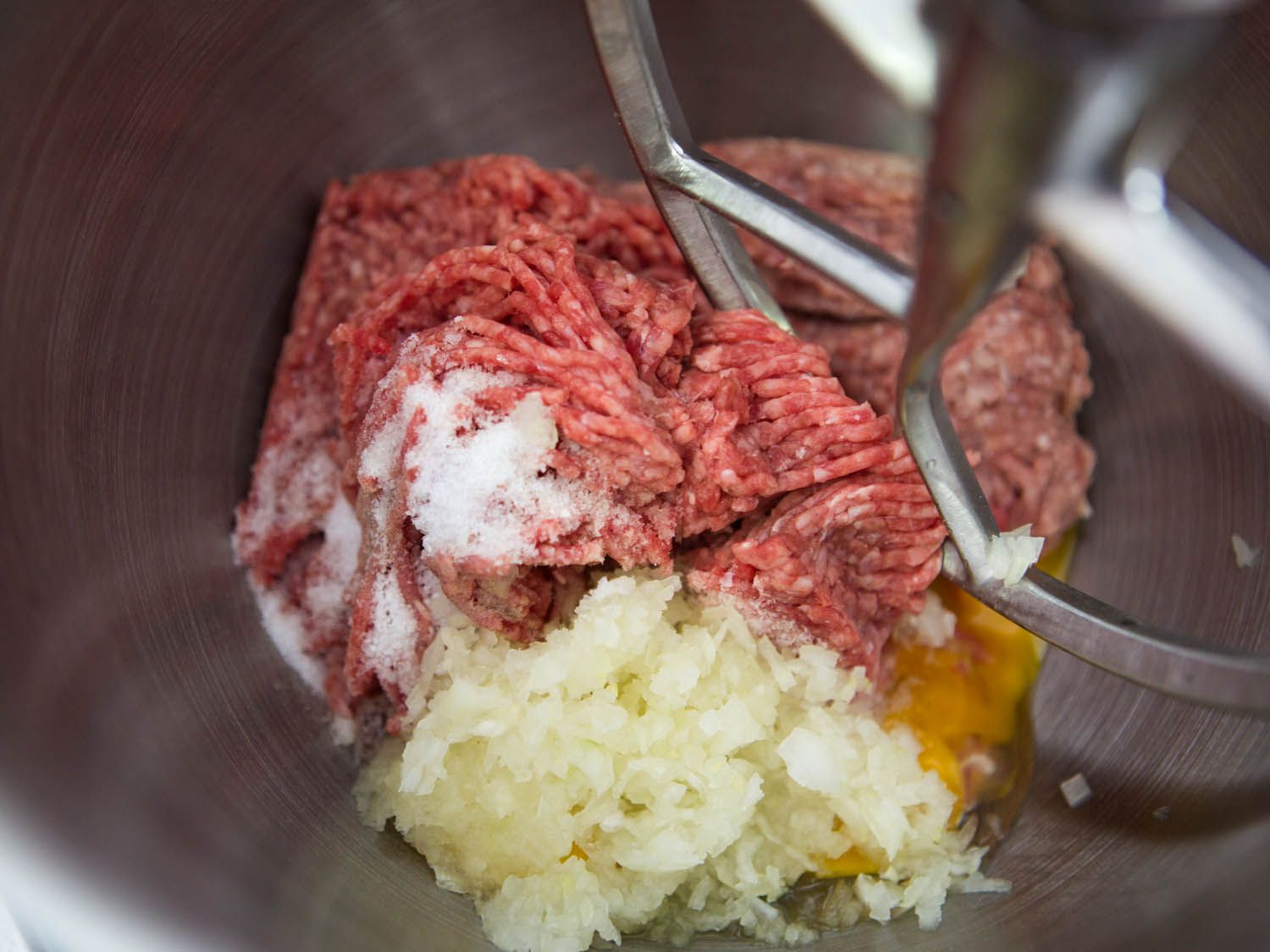 Raw ground beef, pork, salt, eggs, and minced onion in a stand mixer for Swedish meatballs.