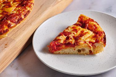 一片新英格兰希腊式披萨，放在有斑点的陶瓷盘子上。在图片的左侧有一个切菜板，上面放着更多的披萨
