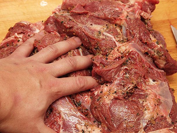 一只手把调味料抹到生的无骨烤羊腿上。