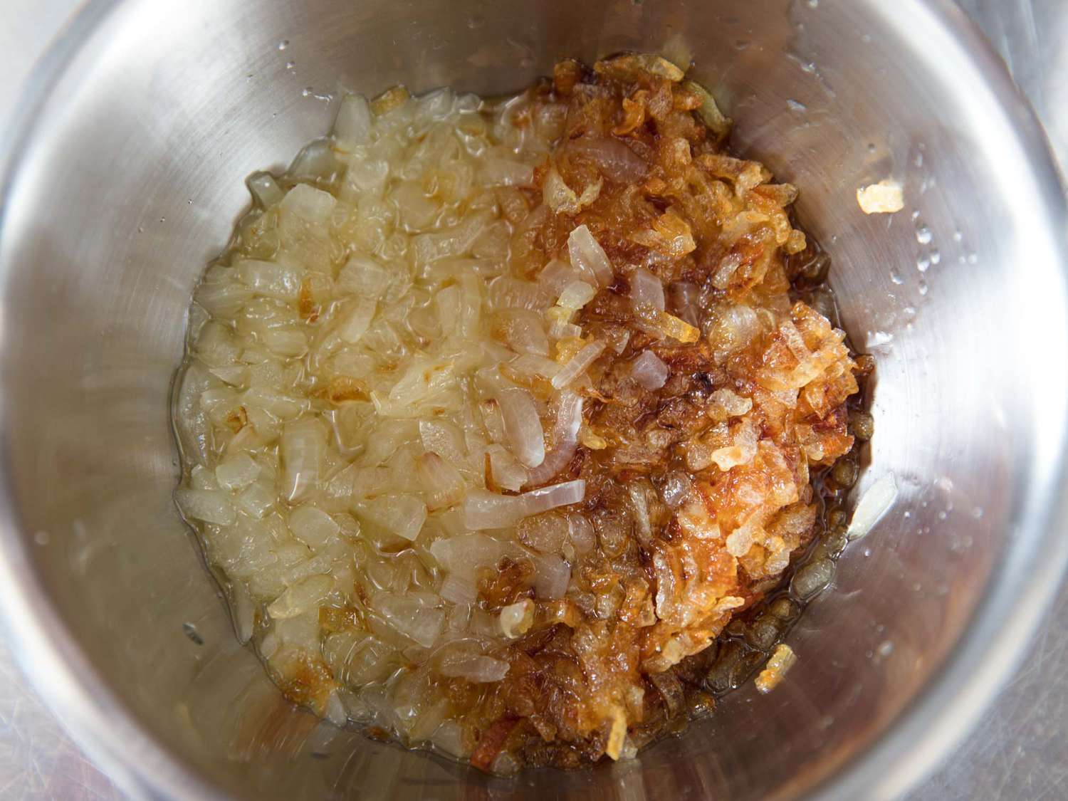 A stainless steel bowl of half onions cooked to light golden, the other half cooked to a deep golden-brown.