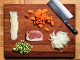 Overhead view of a cutting board showcasing multiple types of cuts of carrots, radishes, onions, meat, and cucumbers