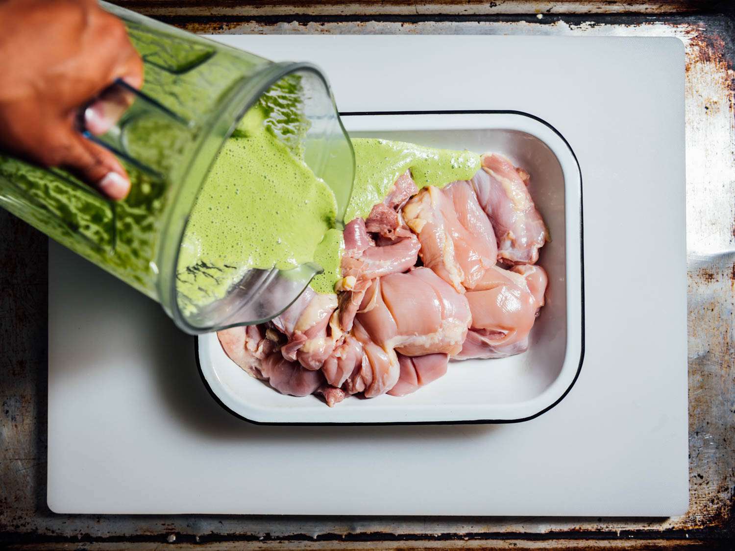 Overhead view of author pouring marinade onto chicken thighs from blender.