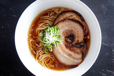 Overhead shot of a bowl of ramen in broth topped with sliced of pressure-cooked pork belly chashu and garnished with sliced scallion.