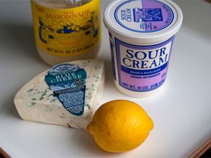一罐酸奶油，一罐蛋黄酱，一整颗柠檬，一块蓝纹奶酪放在砧板上。