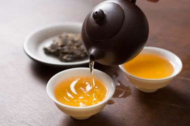 Pu ehr tea being poured from a small black pot into white, handleless cups.