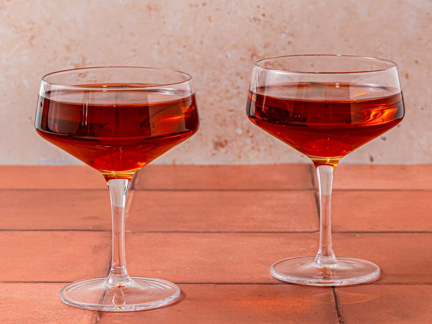 Two Manhattans on a red tiled surface.