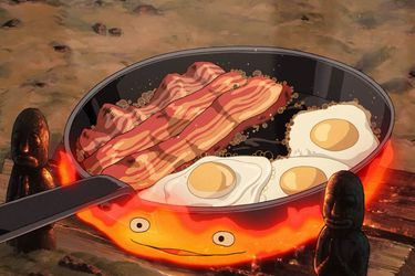 Bacon and eggs cook in a skillet over the flames of Calcifer (a fire demon).