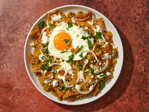 Chilaquiles Verdes topped with a fried egg, on a white plate on a reddish surface.