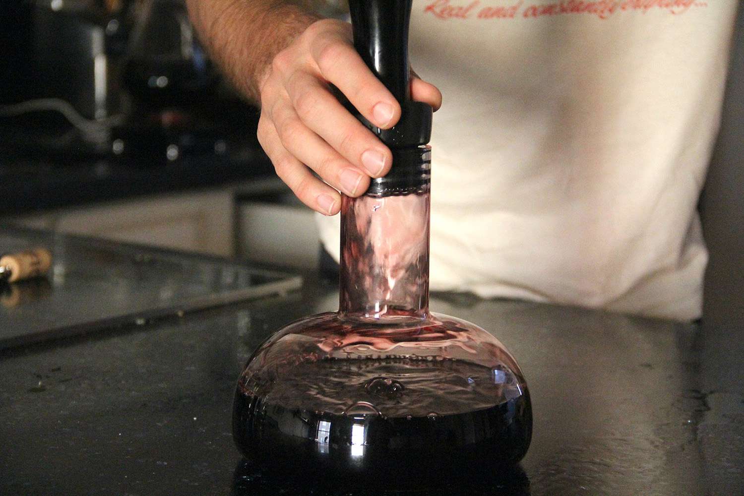 A person holding onto a wine decanter as the wine flows into the base of the decanter