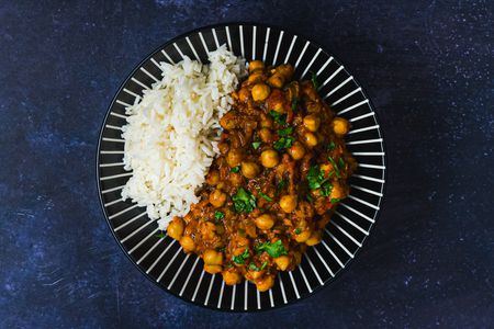 Channa masala and white rice on a blue plate decorated with white lines. The plate is on a dark blue surface.