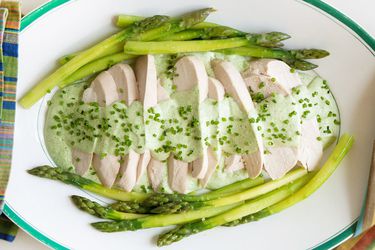 a platter of sliced poached chicken topped with Green Goddess sauce and asparagus spears
