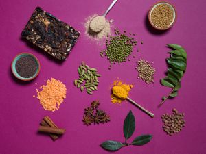 Overhead view of Indian pantry items arranged on a fuchsia surface.