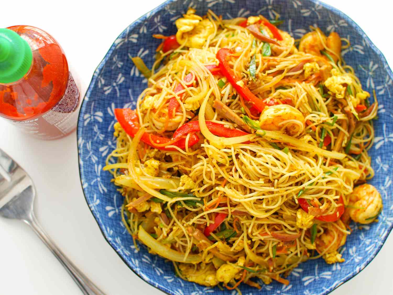 A bowl of curried Singapore rice noodles with char siu, shrimp, bell peppers, and vegetables.