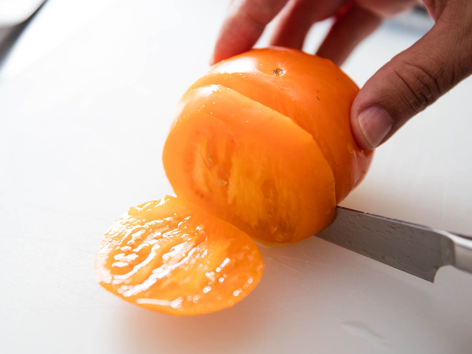 A ripe, yellow tomato variety being sliced on a cutting board.