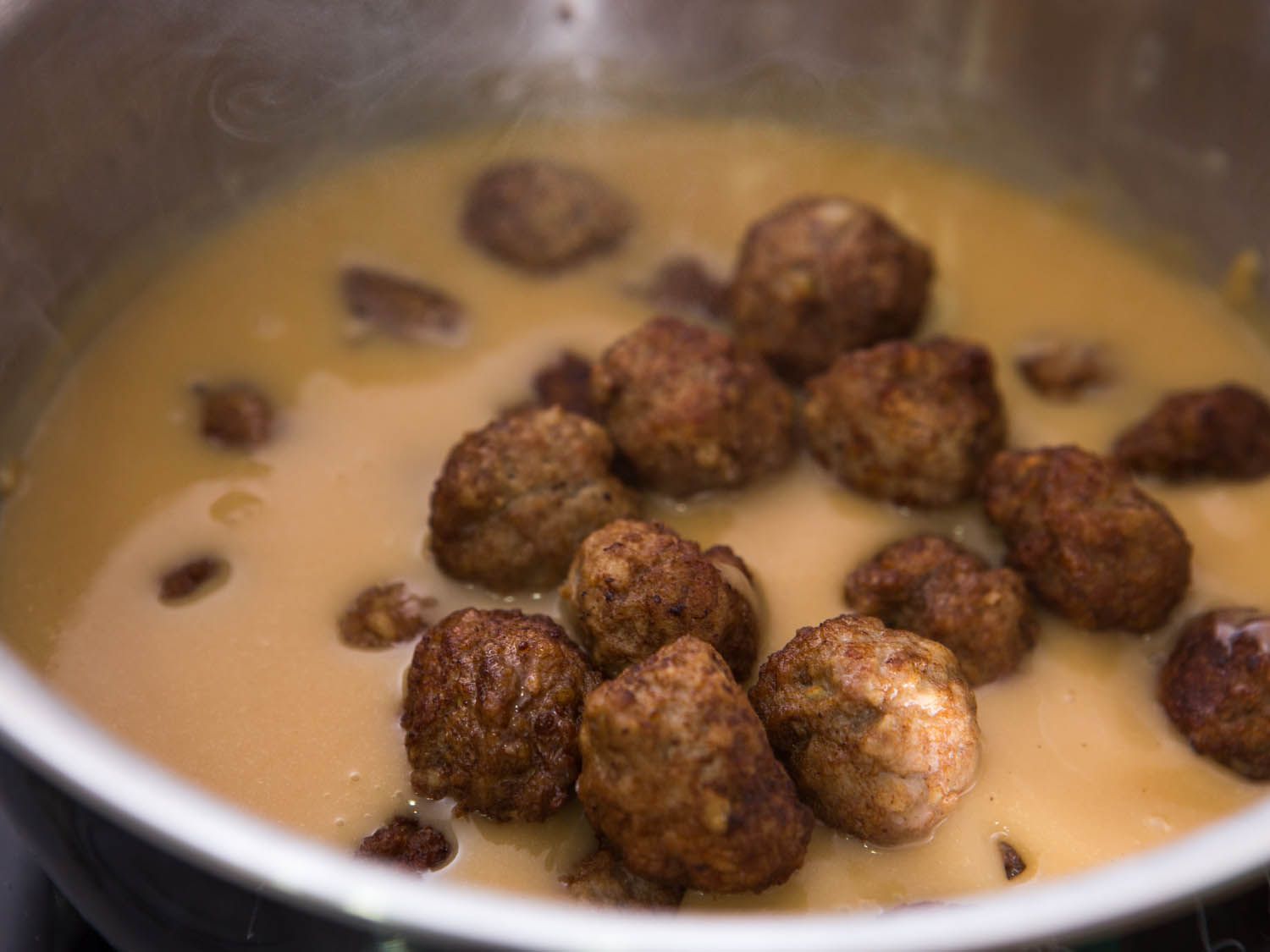 Adding cooked Swedish meatballs into a pot of rich gravy.