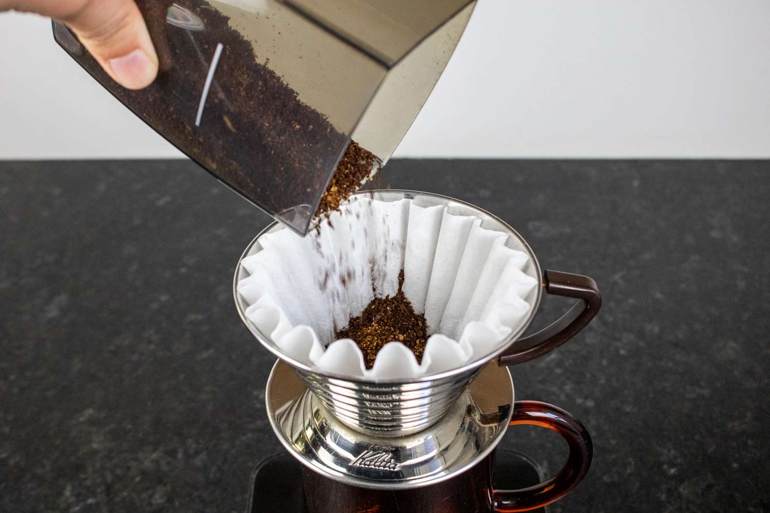 一只手将磨碎的咖啡倒入咖啡机的过滤器中