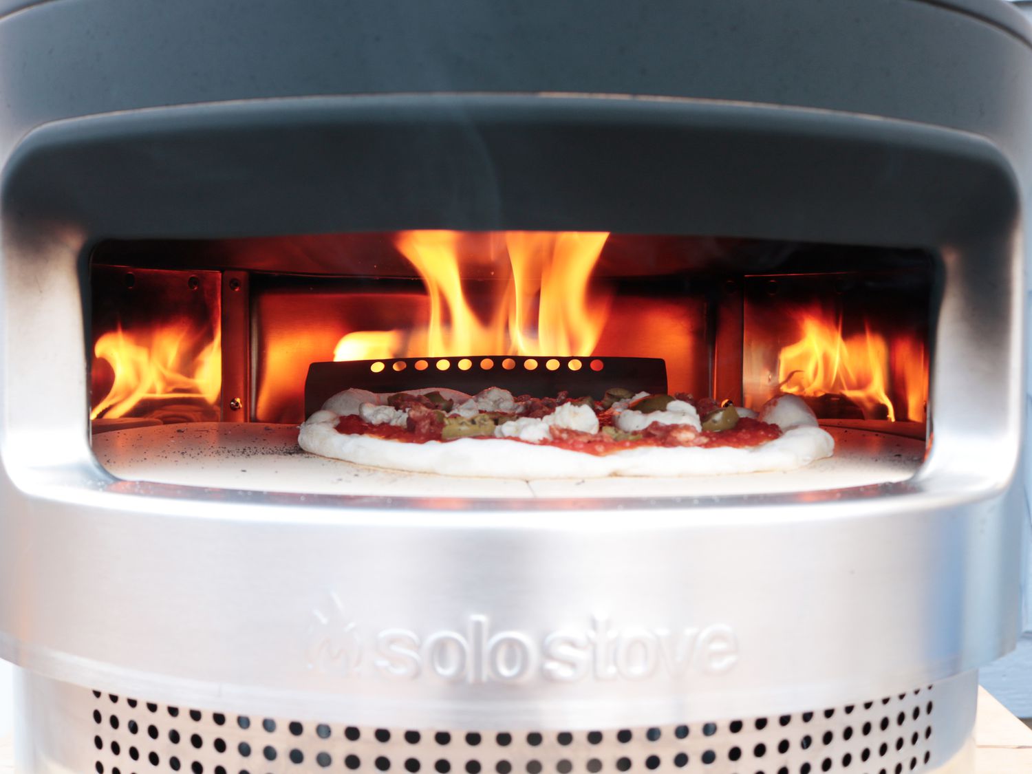 flames coming over the top of a pizza in an outdoor pizza oven