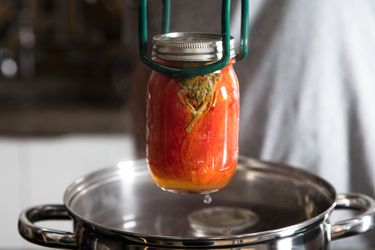 A jar of preserved tomatoes being lifted from a pot of hot water
