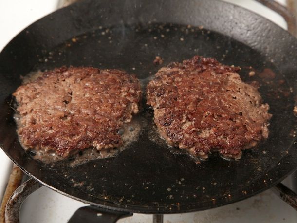 在碳钢煎锅里，两块被砸碎的汉堡肉饼的另一面都烤焦了。